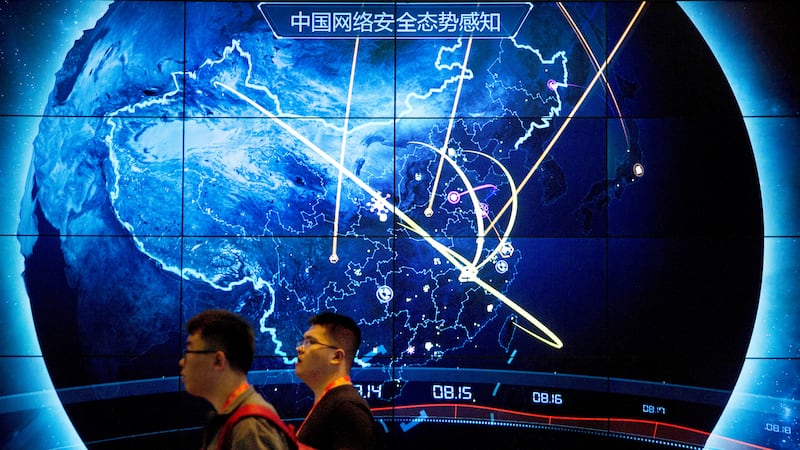 FILE - Attendees walk past an electronic display showing recent cyberattacks in China at the...
